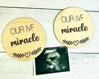 May include: Two round wooden plaques with the words "OUR IVF miracle" in a script font, with a syringe graphic and a heart and leaf design. An ultrasound image is also present.