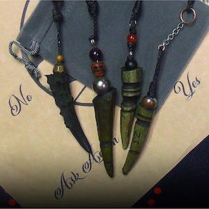 May include: Four handcrafted dowsing pendulums with diverse designs. Each pendulum features a unique combination of beads, wood, and metal accents. The background includes text that reads "No" and "Yes" on a tan surface.