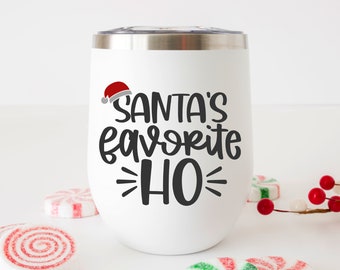 Op de afbeelding: Een witte roestvrijstalen tumbler met een zwart en grijs ontwerp met de tekst "Santa's favoriete HO!" met een rode en witte kerstmanmuts.