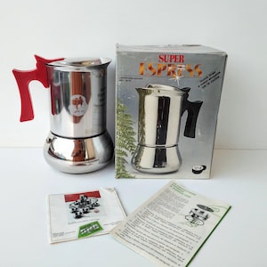Puede incluir: Una cafetera espresso de acero inoxidable con un mango rojo brillante, acompañada de su embalaje de cartón original con la etiqueta Super Espress, junto con dos manuales de instrucciones impresos con diagramas y texto en italiano.