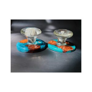May include: Two circular cabinet knobs featuring a combination of natural brown wood burl and vibrant turquoise resin. Each knob is topped with a clear, smooth, mushroom-shaped glass handle that is securely attached to the center of the base.