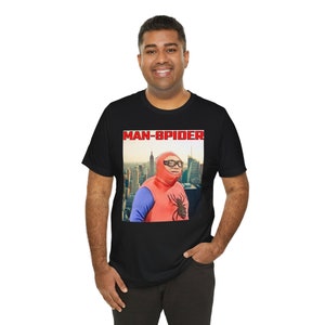 May include: Black t-shirt featuring a graphic of a person in a red and blue superhero costume with the text "MAN-SPIDER" in red letters. The superhero is wearing glasses and a hood, with a cityscape background.