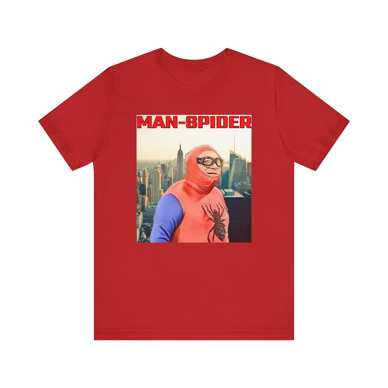 May include: Red t-shirt featuring a humorous image of a person in a homemade Spider-Man costume with the text "MAN-SPIDER" in a red box. The image shows a cityscape in the background.