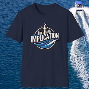 May include: Navy blue t-shirt with a circular graphic featuring an anchor, a cruise ship, and the words "The Implication." The design includes blue and gold wave accents. A boat is visible in the background on the water.