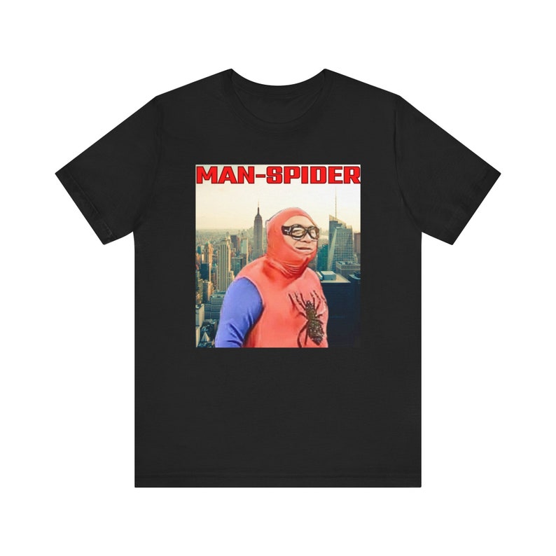 May include: Black t-shirt featuring a retro image of a person in a red and blue superhero costume with the text "MAN-SPIDER" in a red box. The image shows a cityscape in the background.