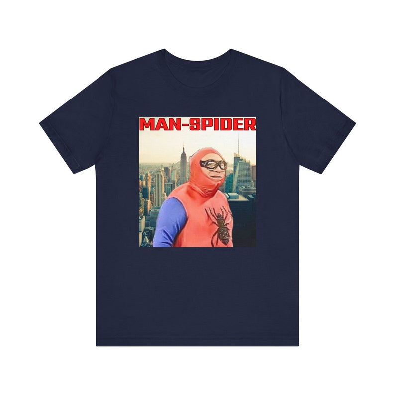 May include: Navy blue t-shirt featuring a humorous image of a person dressed as a superhero with the text "MAN-SPIDER" in red letters. The image shows a cityscape in the background. The superhero costume is red and blue.