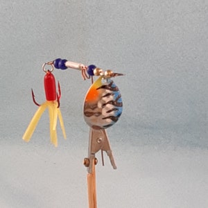 May include: A colourful fishing lure with a blue, orange and white painted blade, a red and yellow feather tail, and a silver hook.