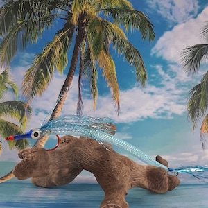 Può includere: Un'esca da pesca a mosca di colore blu chiaro e argento con un occhio rosso e blu, una perla rossa e un amo argentato. L'esca è appoggiata su un pezzo di legno alla deriva con una moneta da un quarto di dollaro americano per la scala.