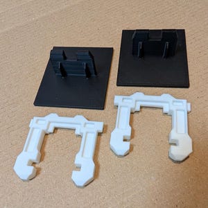 May include: Two white plastic 3D printed parts and one black 3D printed part. The white parts are shaped like a U and the black part is a square base.