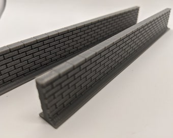 Puede incluir: Dos muros de ladrillo grises en miniatura con una superficie texturizada. Los muros tienen una hilera de ladrillos en la parte superior y están diseñados para mantenerse en pie. Los muros son probablemente para una maqueta o un diorama.