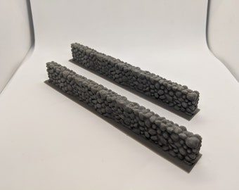 Puede incluir: Dos secciones de muro de piedra gris hechas de pequeñas piedras redondeadas. Las secciones miden aproximadamente 15 cm de largo y 2,5 cm de alto.