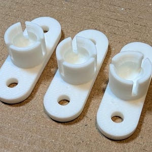Peut inclure: Trois clips de câble en plastique blanc avec un trou rond au centre et une fente sur le côté. Les clips sont conçus pour maintenir les câbles en place.