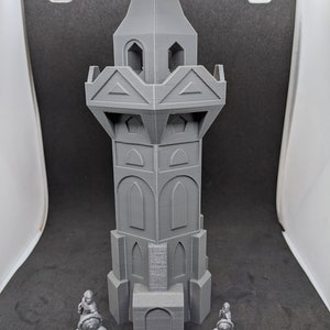 May include: A gray 3D printed tower with a pointed roof and multiple windows. Two gray 3D printed figures stand in front of the tower.