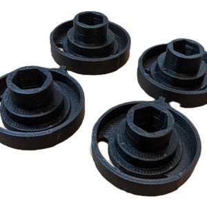 Puede incluir: Cuatro objetos de plástico negro impresos en 3D con un agujero hexagonal central y anillos concéntricos. Los objetos están diseñados para encajar sobre la cabeza de un tornillo.