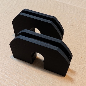 May include: Two black plastic 3D printed cable organisers. The organisers have a U-shaped design with a slot in the middle to hold cables.