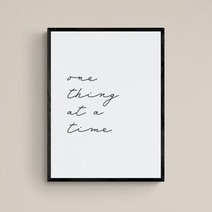 May include: Black framed print with the text "one thing at a time" written in cursive.