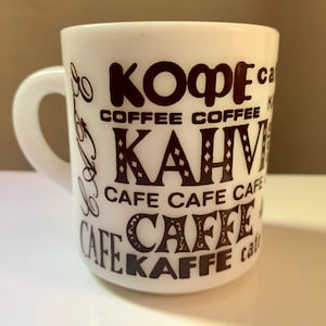 May include: White ceramic coffee mug with a black design that says "Kopf" "Coffee" "Kahve" "Cafe" "Caffe" and "Kaffee" in different languages.