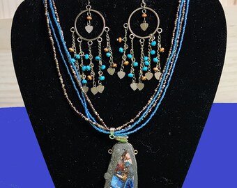 Könnte beinhalten: Eine mehrreihige Halskette mit einem großen, unregelmäßigen Anhänger aus blauem und braunem Stein. Die Halskette besteht aus braunen und blauen Perlen. Die Ohrringe sind silberfarben mit einem Kreisdesign und blauen und braunen Perlen, die von unten hängen.