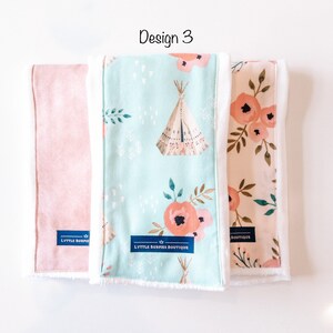 May include: Three burp cloths with different designs. The first is a solid pink, the second is a light blue with a teepee and floral pattern, and the third is a peach with a floral pattern. All three cloths have white trim and a blue label that says "LYTTLE BURPIES BOUTIQUE".