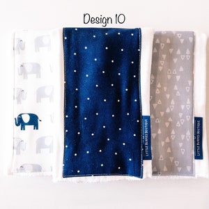 May include: Three fabric burp cloths with different patterns. The first cloth has a white background with gray elephants. The second cloth has a navy blue background with white polka dots. The third cloth has a gray background with white triangles. Each cloth has a white label with the text "Little Burpies Boutique".
