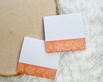 May include: Two white sticky notes with a border of orange and white fall leaves. The notes are on a white fuzzy surface.