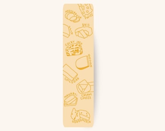 May include: A rectangular bookmark with a light yellow background and illustrations of various cheeses in a golden yellow color. The cheeses include mozzarella, brie, cheddar, and gouda, with their names written next to them.