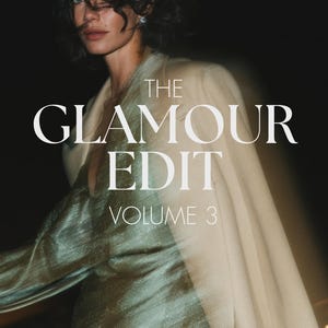 May include: A shimmering sage green dress with a V-neckline paired with a cream-colored blazer draped over the shoulders. The text THE GLAMOUR EDIT VOLUME 3 is centered in white serif font over the clothing against a dark, motion-blurred background.