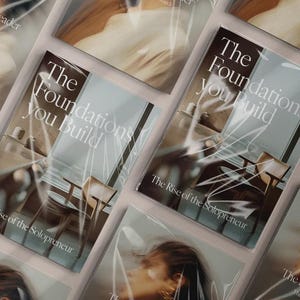May include: Multiple copies of a book titled "The Foundations You Build" are displayed. The book cover features a minimalist interior design image and the text "The Rise of the Solopreneur". The book is wrapped in clear plastic.