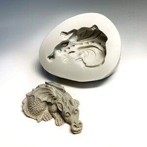 May include: A gray, detailed dragon sculpture and a silicone mold of the dragon. The mold is open and shows the dragon's shape inside.