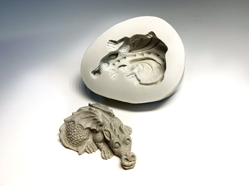 May include: A gray, detailed dragon sculpture and a silicone mold of the dragon. The mold is open and shows the dragon's shape inside.