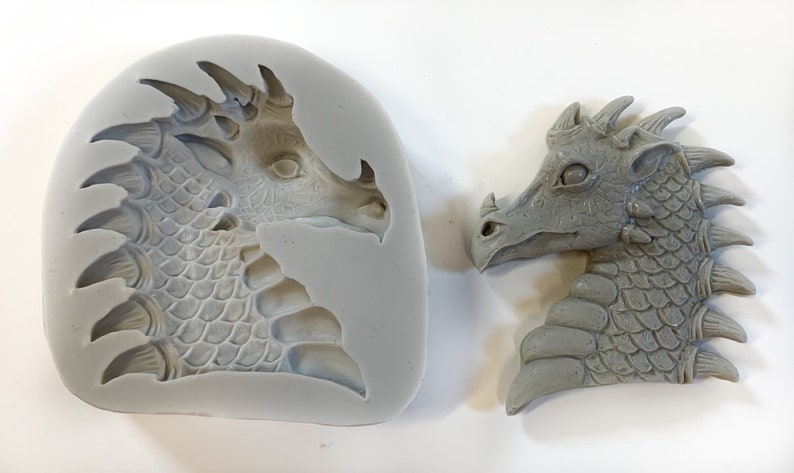 May include: A silicone mold and a gray resin cast of a dragon head. The dragon has a detailed face with scales and spikes.