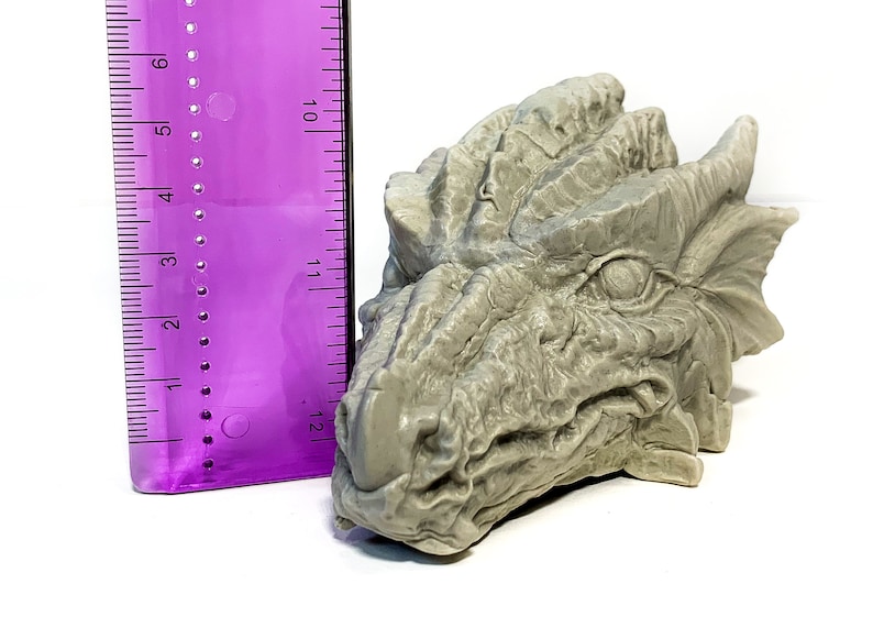 May include: A gray, detailed dragon head sculpture, approximately 5 inches in length, with a textured surface and a realistic appearance.