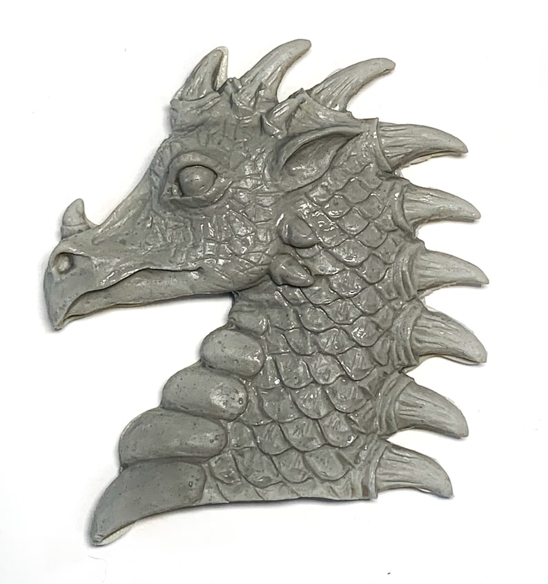 May include: A gray resin dragon head sculpture with detailed scales and spikes. The dragon's head is facing to the side, with its mouth closed and its eyes closed. The sculpture is a great addition to any fantasy or dragon-themed decor.