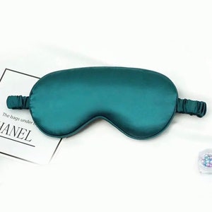 Könnte beinhalten: Eine Schlafmaske aus tealblauer Seide mit einem Gummiband. Die Maske ist so konzipiert, dass sie Licht abhält und den Schlaf fördert.