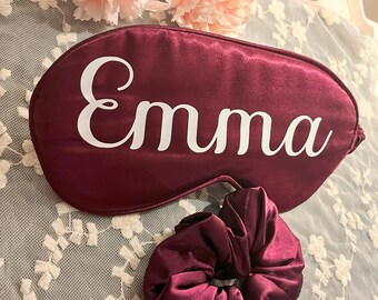 May include: Burgundy satin sleep mask with the name "Emma" embroidered in white. A matching burgundy satin scrunchie is also pictured.