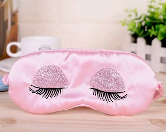 Può includere: Maschera per dormire in raso rosa con ciglia ricamate e dettagli glitter.