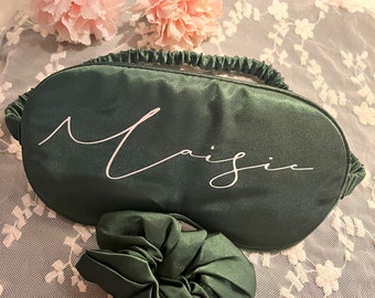 May include: A dark green satin sleep mask with the word "Magic" embroidered in white. A matching dark green satin scrunchie is also included.