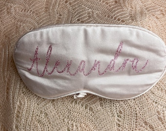 Può includere: Una maschera per dormire in raso rosa con il nome "Alexandra" ricamato in glitter rosa.