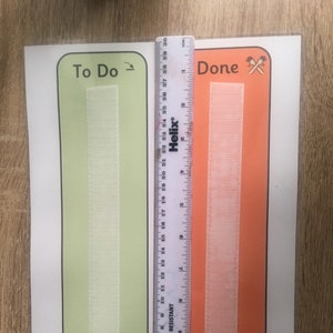 May include: Two white hook and loop fasteners, one on a green background with the text "To Do" and the other on an orange background with the text "Done". A ruler is visible next to the fasteners.