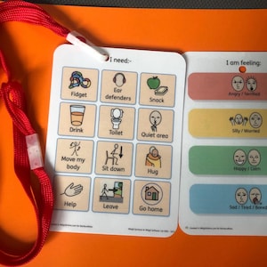 May include: A communication aid with a red lanyard. The board is split into two sections: "I need:" with icons representing needs, and "I am feeling:" with emotion indicators. The board is designed to assist communication.