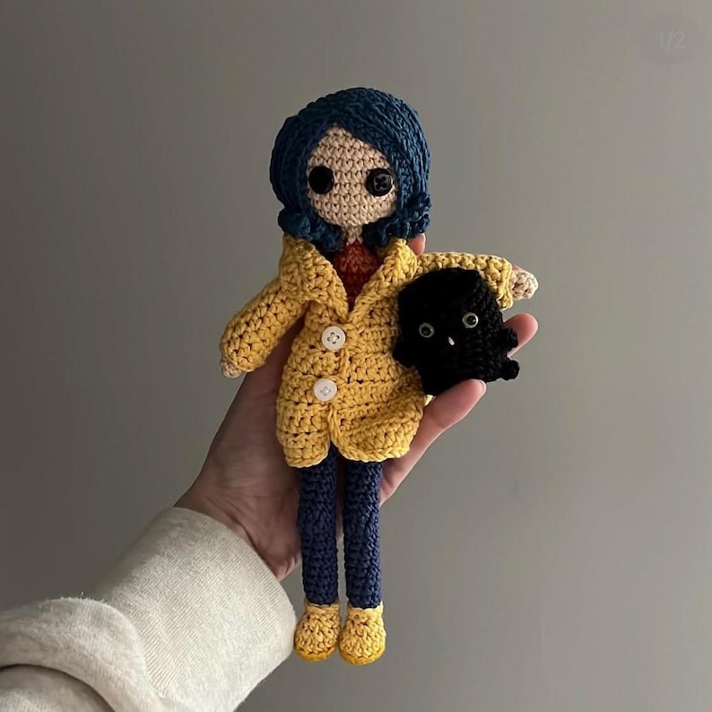 May include: A handmade crochet doll with blue hair, a yellow coat, and blue pants. The doll is holding a black creature. The doll has button eyes and a red shirt. The doll's shoes are yellow.