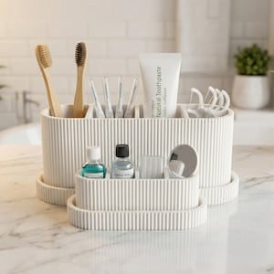Könnte beinhalten: Ein weißes, ovales Badezimmer-Organizer-Set mit gerippter Textur. Der größere Behälter enthält zwei Bambuszahnbürsten, vier Interdentalbürsten, eine Tube Natural Toothpaste und Zahnseide-Sticks. Ein kleineres passendes Tablett enthält Mundwasser.