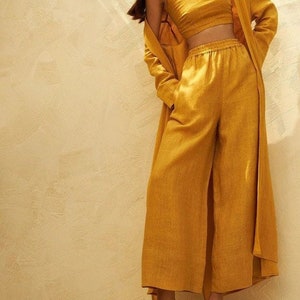 May include: A mustard yellow linen pantsuit with a cropped top and a long cardigan. The outfit is styled with simple sandals.