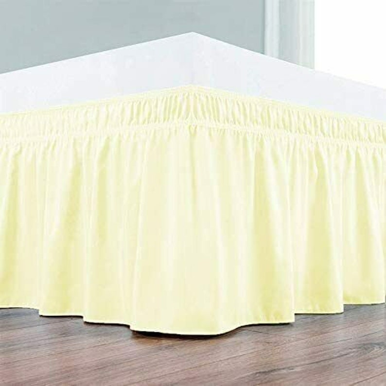 May include: A pale yellow bed skirt with a ruffled edge. The skirt is made of a soft, smooth fabric and is designed to cover the box spring of a bed.