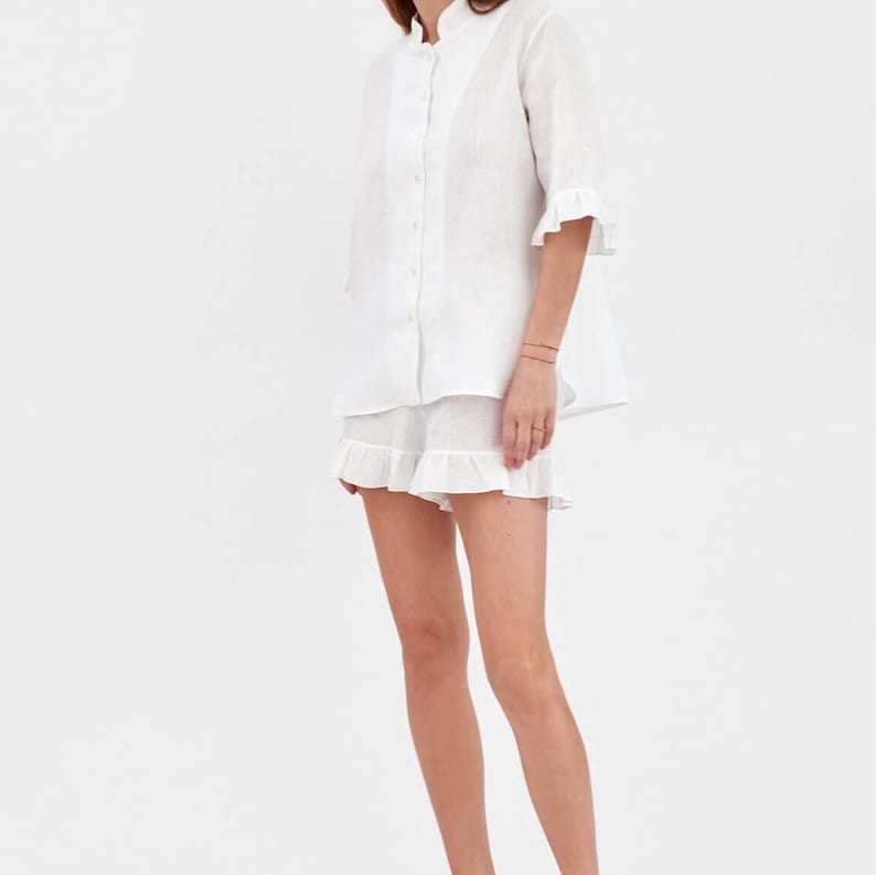 May include: White linen pajama set with a ruffled hem on the shorts and sleeves. The top has a mandarin collar and button closure.