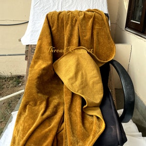 Pu&ograve; includere: Coperta in velluto color senape drappeggiata su una sedia. La coperta ha un aspetto morbido e strutturato ed &egrave; piegata per rivelare un lato inferiore giallo pi&ugrave; chiaro. Le parole "Thread Connect" sono visibili sulla coperta.