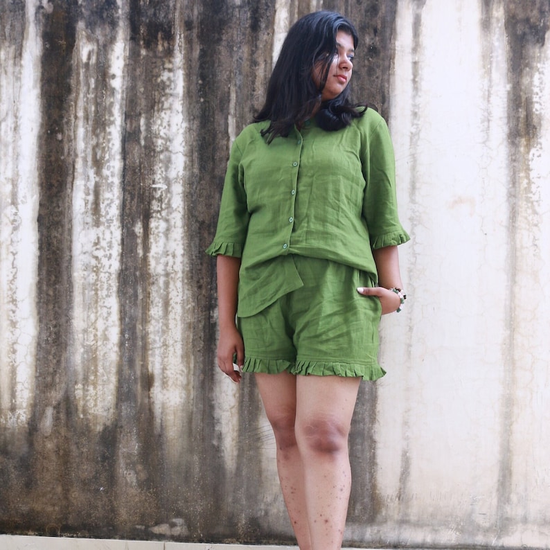 May include: A green linen short set with a button-up top and ruffled trim. The top has a collar and short sleeves. The shorts have a high waist and are also ruffled.