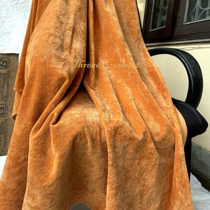 Pu&ograve; includere: Una coperta in velluto arancione bruciato drappeggiata. Il tessuto &egrave; morbido e soffice, con texture e pieghe visibili. La coperta &egrave; drappeggiata su una sedia nera. Il testo "Thread Connect" &egrave; visibile.