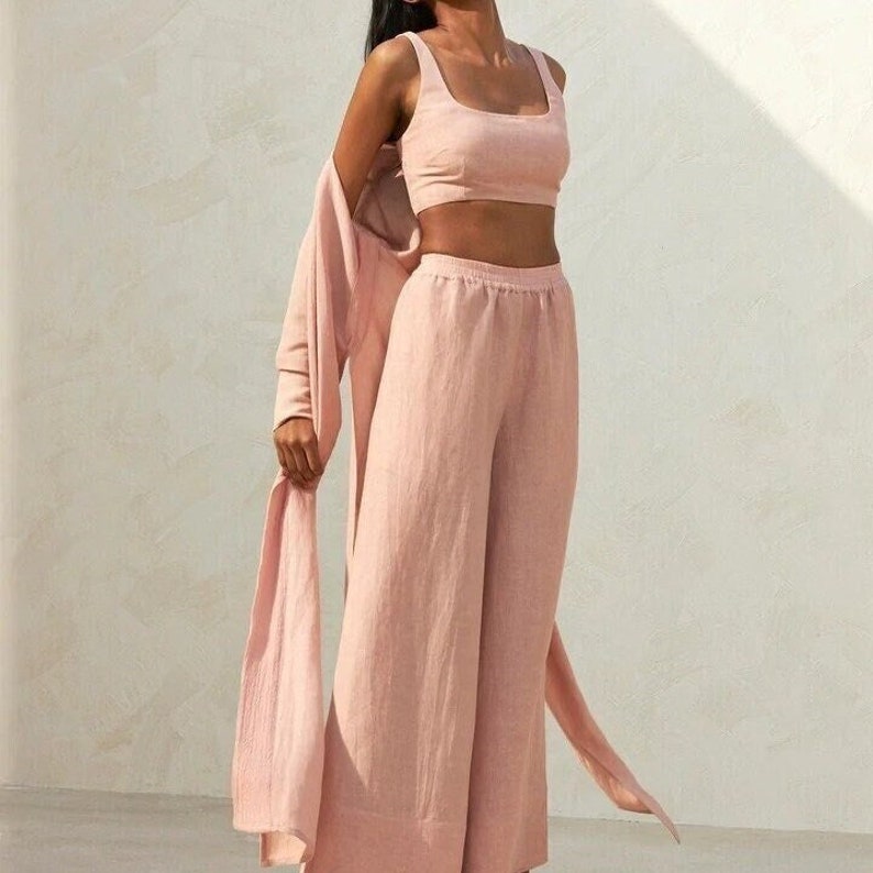 May include: A blush pink linen pantsuit with a cropped top and wide-leg pants. The pants have a drawstring waist.