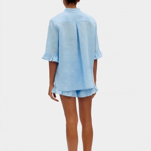 May include: A light blue linen shirt and shorts set with ruffle detailing. The shirt has a button-up front and short sleeves. The shorts have a relaxed fit and a ruffle trim.